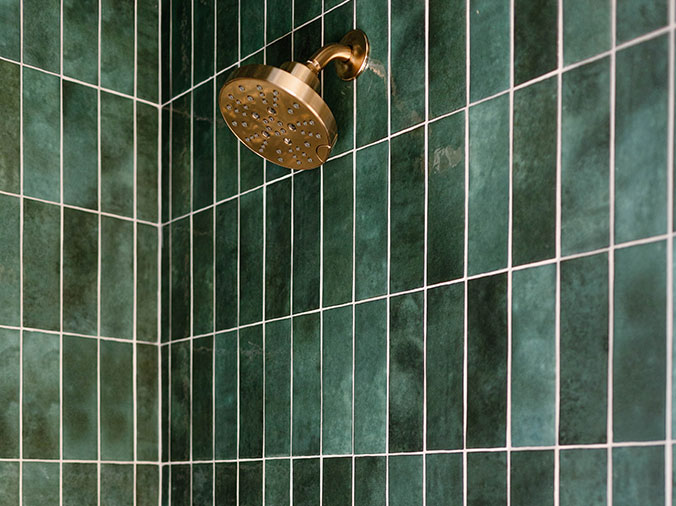Bronze shower head with green tile background