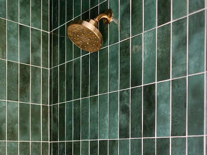 Bronze shower head with green tile background